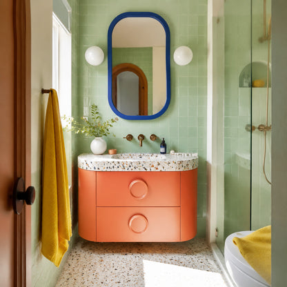 Small bathroom with pastel green tiles coral vanity and blue mirror